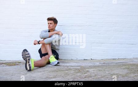 Eine gute Dehnung. Ein sportlicher junger Mann, der seine Beine vor dem Training streckt. Stockfoto