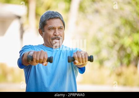 Stark und aktiv bleiben. Ein reifer Mann hebt Hanteln draußen. Stockfoto