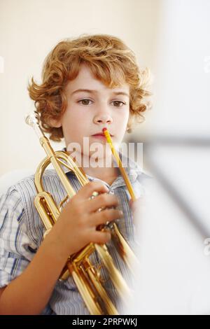 Von Spielzeug zu Trompeten. Ein niedlicher kleiner Junge spielt Trompete. Stockfoto