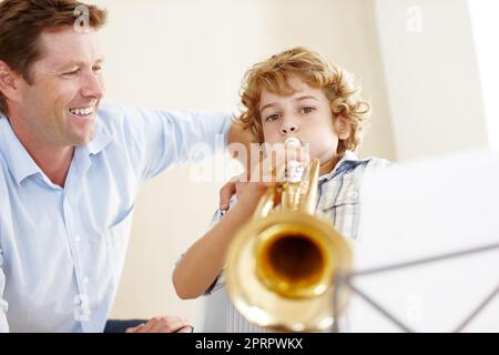 Ein süßer kleiner Junge spielt die Trompete, während sein Vater ihm stolz zuschaut. Stockfoto