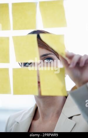 Visualisieren ihrer Gedanken. Eine Geschäftsfrau arrangiert Haftnotizen auf einem Glaswal. Stockfoto