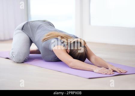 Linderung ihrer täglichen Belastungen. Eine junge Frau, die auf ihrer Trainingsmatte Yoga macht. Stockfoto