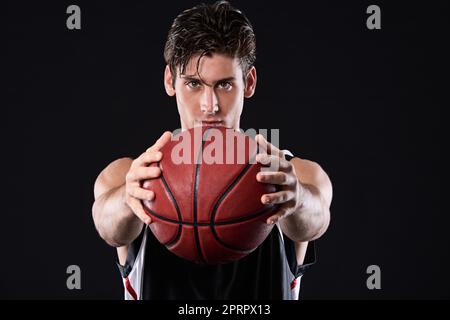 Ich fordere Euch heraus. Beschnittenes Studioporträt eines entschlossenen Basketballspielers, der den Ball vor sich hält. Stockfoto