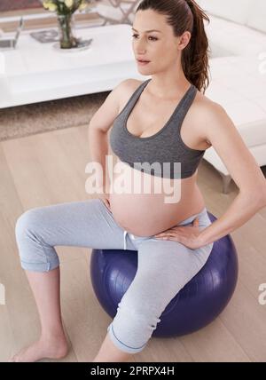 Training für zwei. Eine junge Schwangerin trainiert zu Hause. Stockfoto