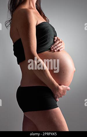 Sie erwartet ihre baldige Ankunft. Eine Schwangere hält ihren Bauch. Stockfoto