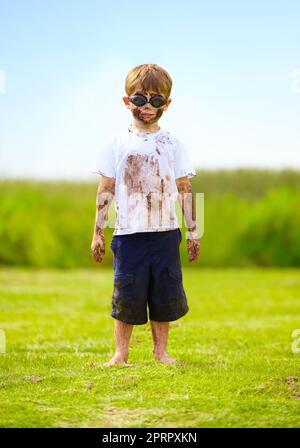 Ein schlammiger Superheld. Ein kleiner Junge, der als Superheld verkleidet und mit Schlamm bedeckt ist. Stockfoto