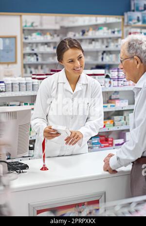 Sie sorgt immer dafür, dass die Kunden ihre Medikamente kennen. Eine junge Apothekerin hilft einem älteren Kunden an der Rezeptheke. Stockfoto