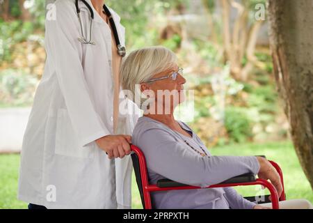 Unterstützung für die Genesung von Patienten. Eine ältere Frau im Rollstuhl wird von ihrem Arzt gedrängt. Stockfoto