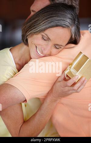 Zeigt ihre Wertschätzung. Eine attraktive reife Frau umarmte ihren Mann, nachdem sie ein Geschenk von ihm erhalten hatte. Stockfoto