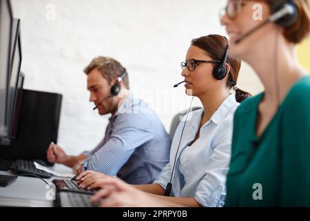 Bearbeitung von Kundenanfragen. Eine Gruppe von Kundendienstmitarbeitern, die Anrufe an ihren Computern entgegennehmen. Stockfoto