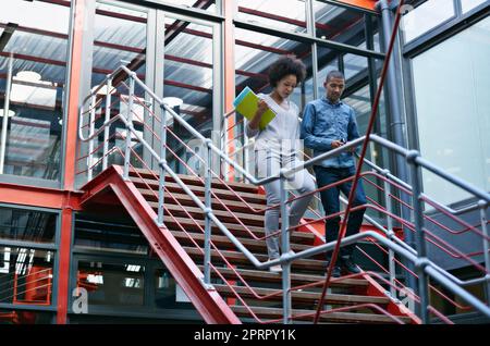 Auf dem Weg zu einem Meeting. Zwei Kollegen, die in ihrem Gebäude nebeneinander die Treppe hinunter laufen. Stockfoto