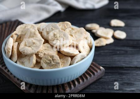 Schüssel mit getrockneten Bananenscheiben auf schwarzem Holztisch, Nahaufnahme Stockfoto