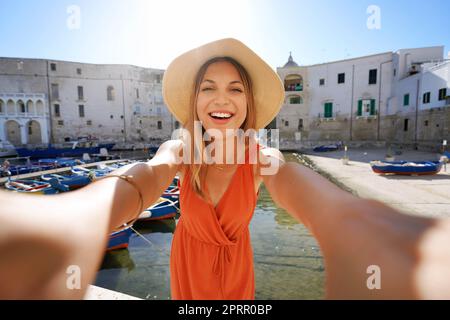 Selfie-Mädchen in Süditalien. Junge Touristenfrau, die sich mit dem alten Hafen von Monopoli, Apulien, Italien, porträtiert. Stockfoto