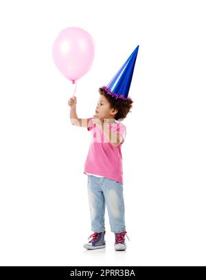 Ich Frage mich, ob ich auf dieser Sache wegschweben könnte...Studioaufnahme eines niedlichen kleinen Mädchens, das einen Partyhut trägt und einen Ballon vor einem weißen Hintergrund hält. Stockfoto