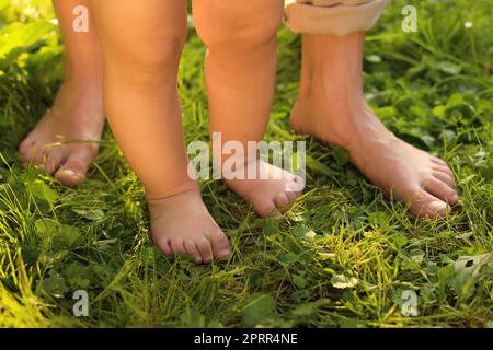 Eine Frau mit ihrem Kind, die barfuß auf grünem Gras im Freien läuft, Nahaufnahme Stockfoto