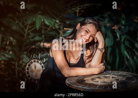 Schöne junge Latina Frau sitzt an einem Tisch mit Dschungel-Typ Hintergrund Stockfoto