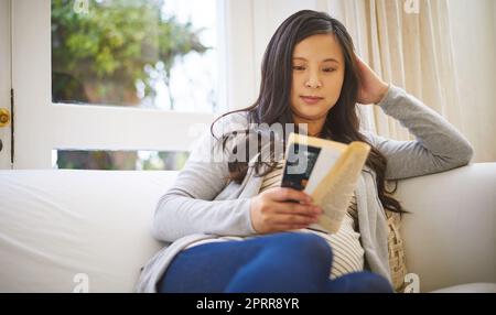 Ich lese über das kleine Ding der Schwangerschaft. Eine schwangere Frau, die zu Hause ein Buch liest Stockfoto