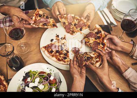 Das Essen ist serviert. Ein Foto aus einem hohen Winkel, bei dem eine Gruppe von nicht wiedererkennbaren Personen sich jeweils ein Stück Pizza schnappt, während sie in einem Restaurant sitzen Stockfoto