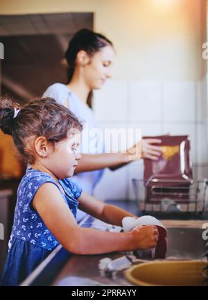 Mommys kleine Helferin. Ein glückliches kleines Mädchen und ihre Mutter waschen zu Hause zusammen das Geschirr Stockfoto