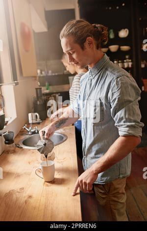 Es gibt nichts Besseres als einen frischen Becher, um den Tag zu beginnen. Ein hübscher junger Mann gießt ein Warngetränk. Stockfoto