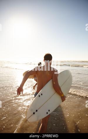 Geht ins Brandung. Rückansicht eines jungen Surferpaares, das zusammen ins Meer läuft. Stockfoto