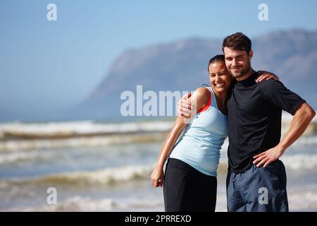 Wir lieben es, unser Sommertraining zu teilen. Ein liebevolles junges Paar posiert in Sportkleidung am Strand. Stockfoto