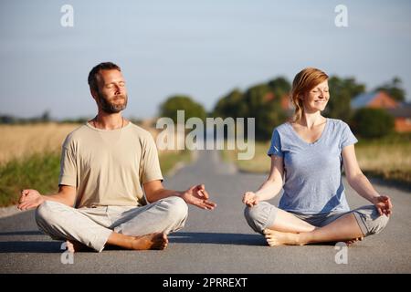 Ein ruhiges Paar, das in der Lotusposition auf einer Landstraße sitzt. Stockfoto