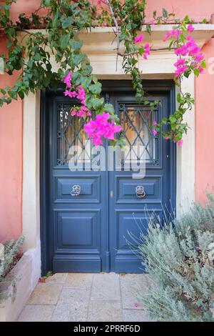 Traditionelles griechisches Haus mit Blumen auf der Insel Korfu, Griechenland. Blaue Tür, umgeben von magentafarbenen Blumen Stockfoto