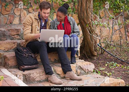 Ein junges Paar, das auf dem Campus einen Laptop benutzt. Stockfoto