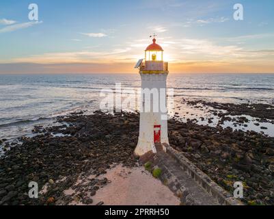 Blick aus der Vogelperspektive auf den Sonnenaufgang hinter einem weißen Leuchtturm an einer felsigen Küste auf Griffith's Island bei Port Fairy an der Great Ocean Road in Victoria, Australien Stockfoto