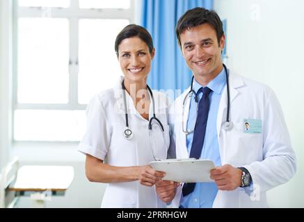 Sie stehen oben auf diesem Fall. Porträt eines lächelnden medizinischen Teams, das die Patientenakte überprüft. Stockfoto