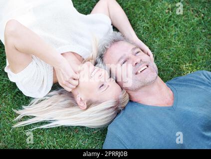 Ich bin so dankbar für Euch. Ein reifer Mann, der mit seiner Frau auf dem Gras liegt und nachdenklich nach oben blickt. Stockfoto