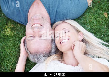 Das ist einfach super. Ein reifes Paar liegt auf dem Gras und lächelt mit geschlossenen Augen. Stockfoto