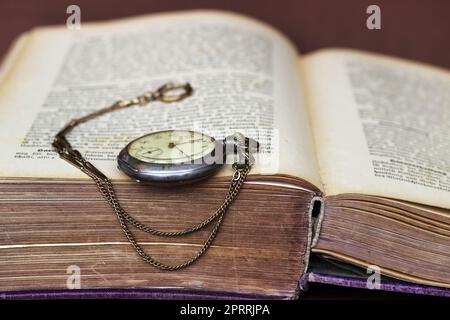 Eine antike Taschenuhr lehnt sich an ein altes Buch mit Vergilbte Seiten Stockfoto