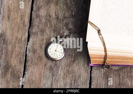 Eine antike Taschenuhr und ein altes Buch auf einem alten Holztisch Stockfoto