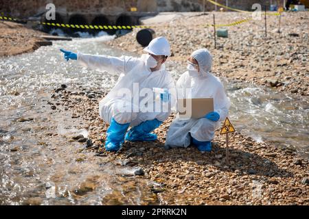 Biologe tragen Schutzanzug und Maske sammelt Abwasserproben aus der Industrie Stockfoto