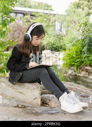 Junge Mädchen lesen Buch und Musik im Park hören Stockfoto