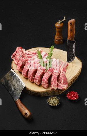 Rohe Lammrippenbraten auf Holzplatte und Fleischerbeil Stockfoto