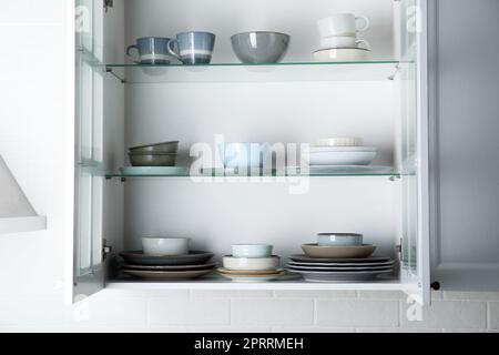 Offener Schrank mit verschiedenen sauberen Tellern und Schüsseln in der Küche Stockfoto