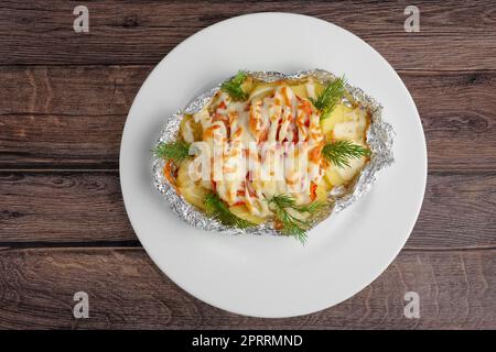 Blick von oben auf gebratenen Meeresfisch und Kartoffeln mit Paprika und Käse auf einem Holztisch Stockfoto