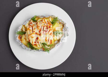 Blick von oben auf gebratenen Meeresfisch und Kartoffeln mit Paprika und Käse auf grauem Hintergrund Stockfoto