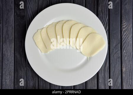 Blick von oben auf Mozzarella-Käsescheiben auf einer runden Platte auf einem Holztisch. Stockfoto