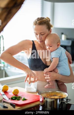 Frau kocht, während sie ihren vier Monate alten Jungen in den Händen hält Stockfoto