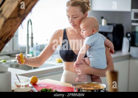 Frau kocht, während sie ihren vier Monate alten Jungen in den Händen hält Stockfoto