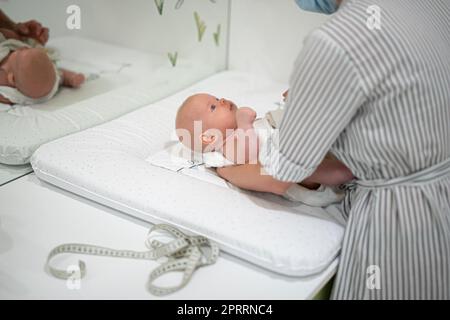 Baby liegt auf seinem Rücken und wird während einer normalen medizinischen Untersuchung vertagt. Stockfoto