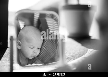 Schöne Aufnahme eines niedlichen Jungen, der seine Spiegelung im Spiegel betrachtet. Schwarzweiß-Bild. Stockfoto