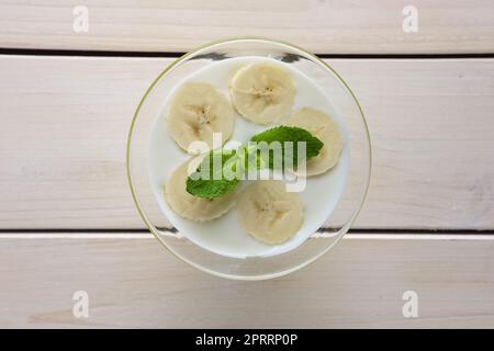 Blick von oben auf Glas mit Joghurt und rohem Honig, garniert mit Bananen und Minzeblättern Stockfoto