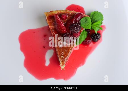 Blick auf Käsekuchen mit Kirsche, Erdbeere und Taubeere, dekoriert mit Sirup und Minzblättern Stockfoto