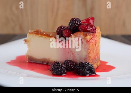 Ein Stück Käsekuchen mit Kirsche, Erdbeere und Taubeere, dekoriert mit Sirup Stockfoto