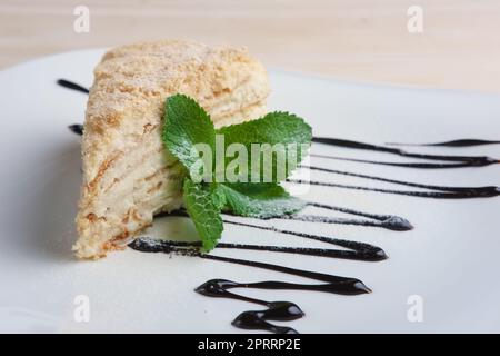 Ein Stück napoleonkuchen auf einem Teller mit Schokoladensoße. Blätterkuchen mit Pudding Stockfoto